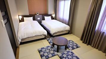 A hotel room with two beds, a small table, and a view of the outside through the window.