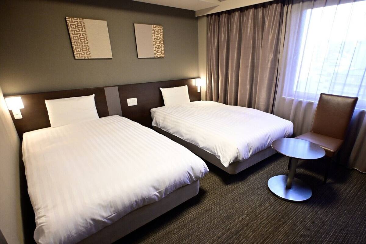 A hotel room with two beds, a small round table, and a chair.