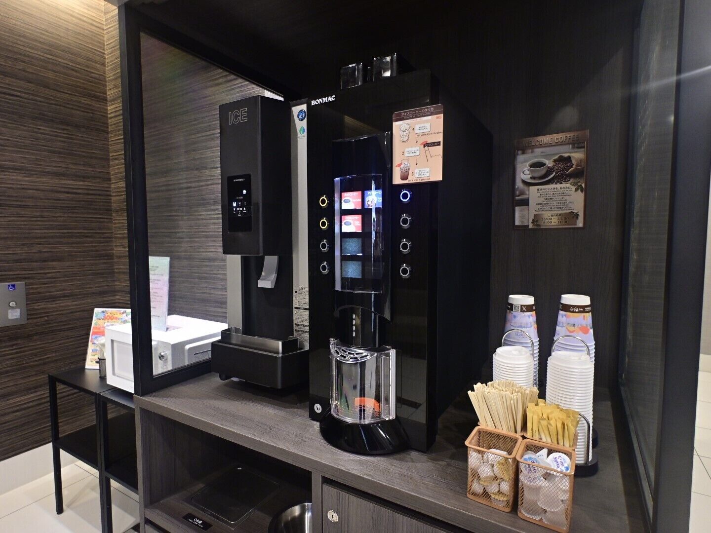 A coffee station with an ICE machine, a BONMAC coffee machine, and a coffee dispenser. There are disposable cups and a basket of napkins.