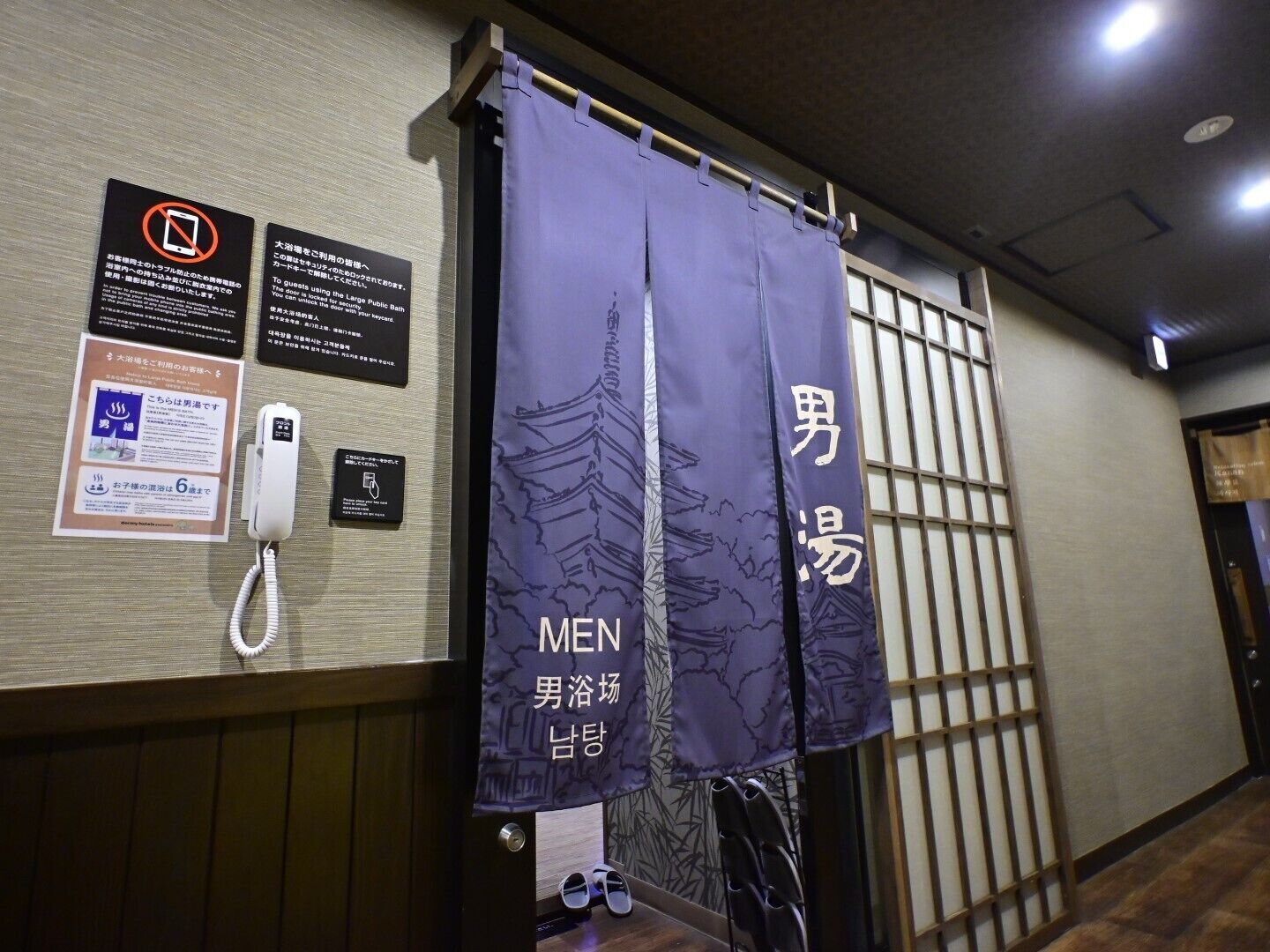 A men's bathroom with a phone, informational signs, and a curtain with Japanese text.