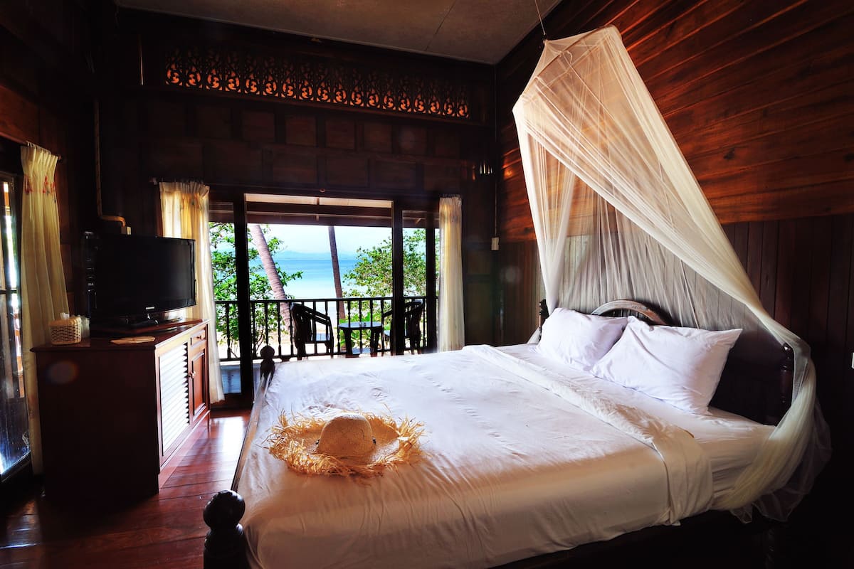 A bedroom with a bed, a television on a wooden cabinet, and a view of the outdoors.