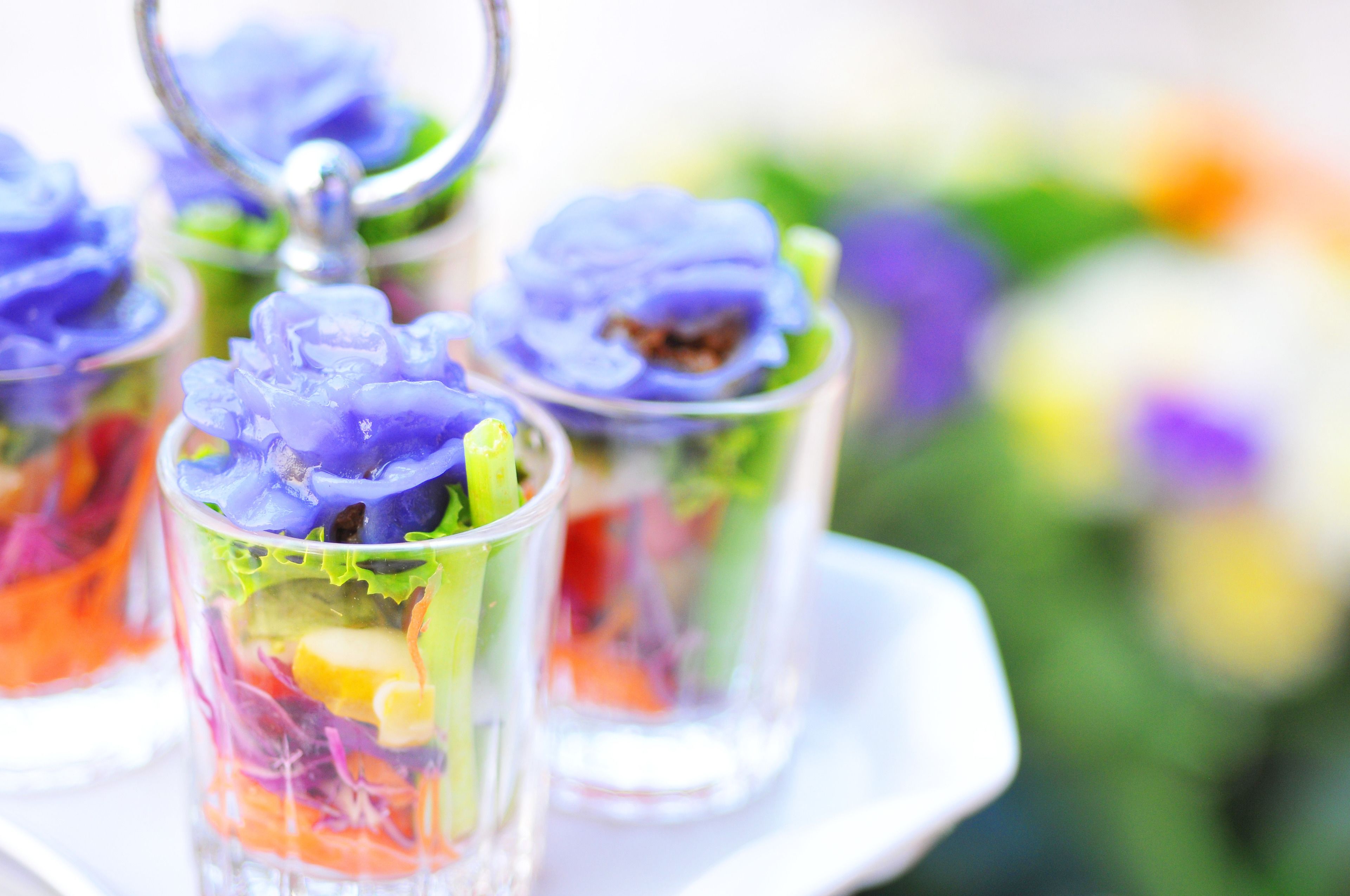 Un vassoio con bicchieri di vetro che contengono insalate colorate guarnite con fiori viola.