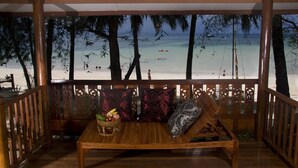 A wooden bench with cushions and a woven basket of fruits, overlooking a beach with palm trees and a clear view of the ocean. - Koh Talu Island Resort (Bang Saphan Noi)