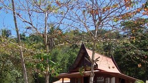A wooden house with a thatched roof, surrounded by trees and a sandy beach. - Koh Talu Island Resort (Bang Saphan Noi)