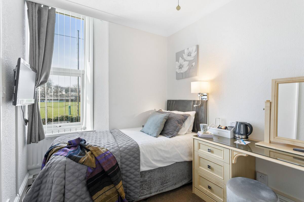 A bedroom with a bed, bedside table, lamp, and a window with curtains.