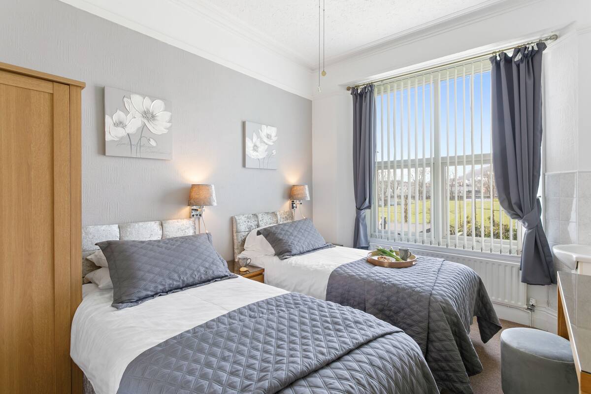 A bedroom with two beds, a wooden wardrobe, and a window with curtains.