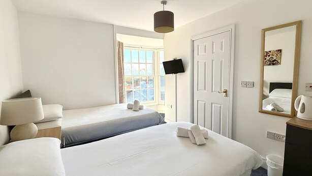A hotel room with two beds, a TV, a mirror, and a window with a view. - The Brunswick Hotel (Bridlington)