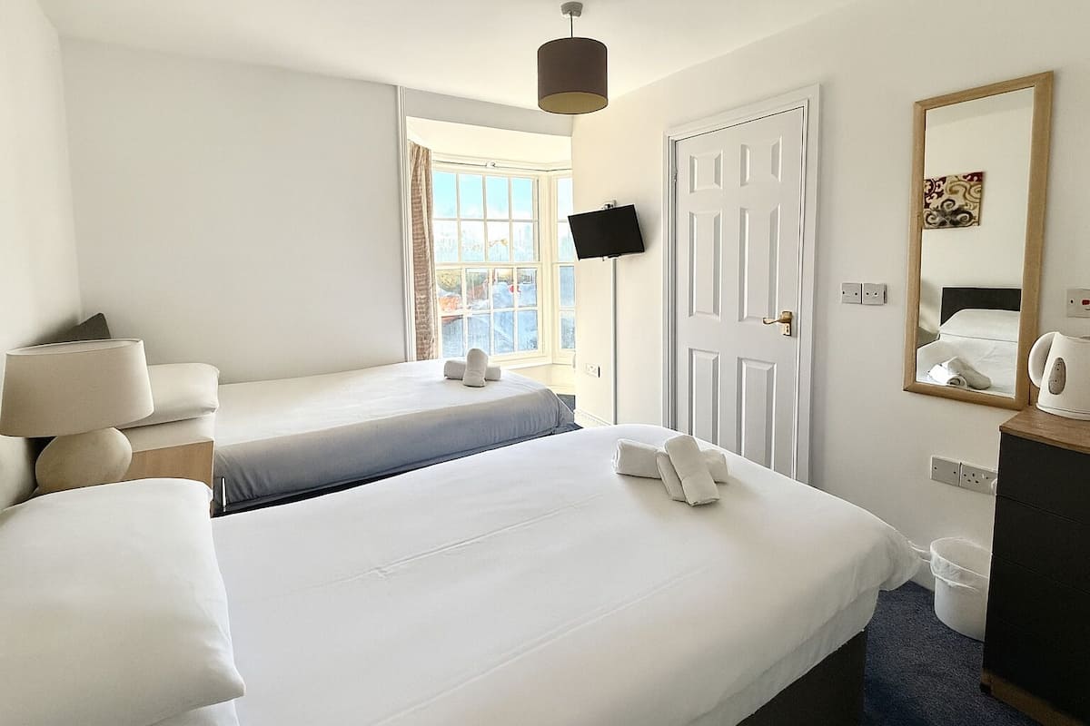 A hotel room with two beds, a TV, a mirror, and a window with a view.