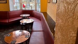 A corner seating area with a red cushioned bench and two round tables with metal tops. - The Brunswick Hotel (Bridlington)