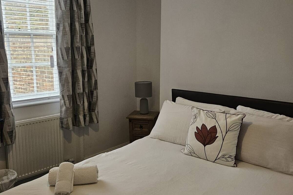 A neatly made bed with white linens, a pillow with a leaf pattern, and a lamp on a bedside table.