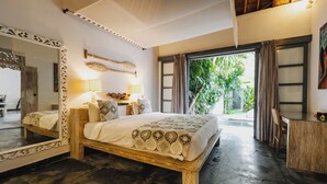 A spacious bedroom with a large bed, a wooden headboard, a mirror, and a view of the outdoors.