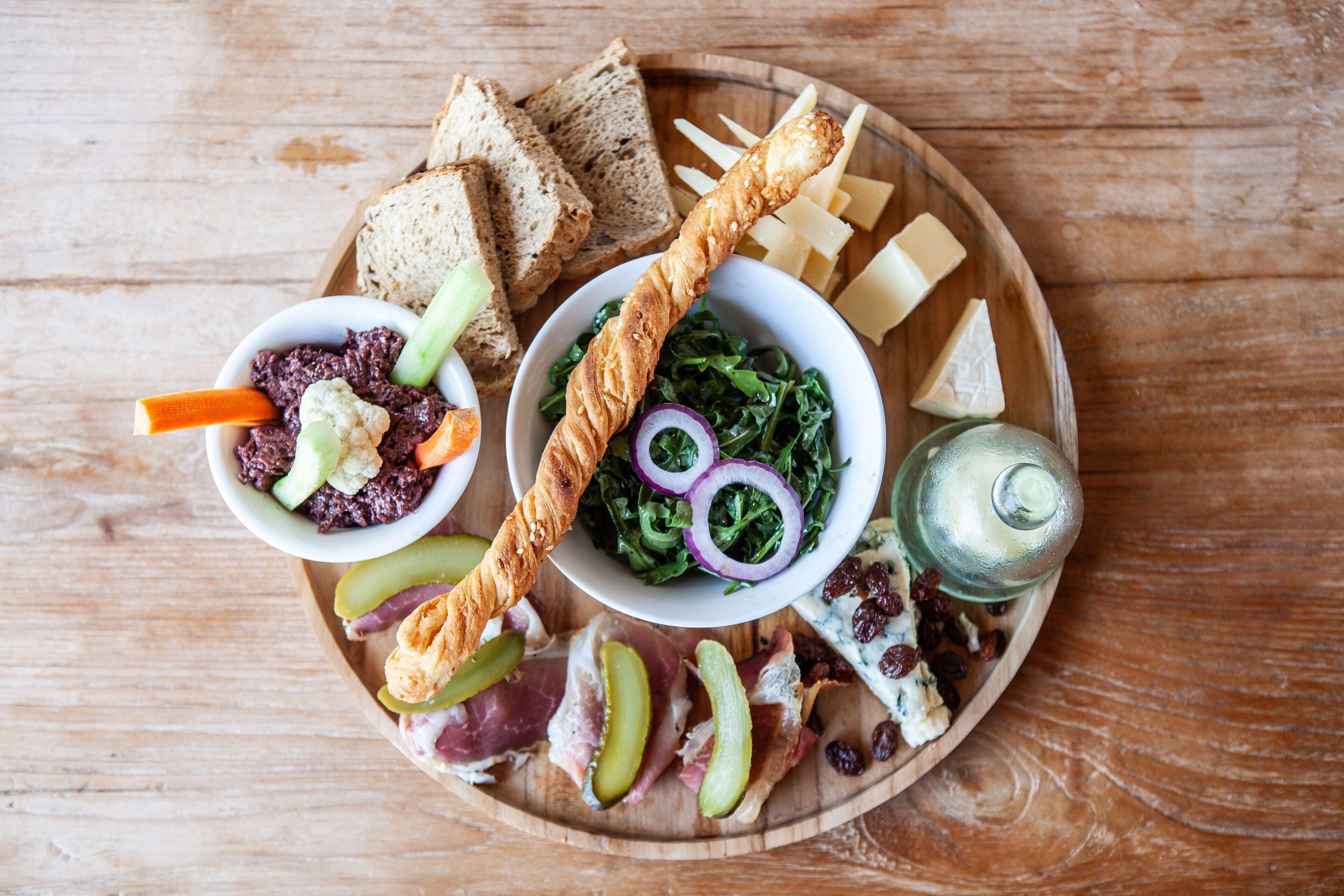 Una tabla de madera con diversos alimentos, entre ellos pan, queso y una ensalada.