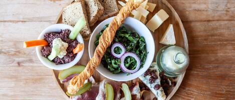 Una tabla de madera con diversos alimentos, entre ellos pan, queso y una ensalada.