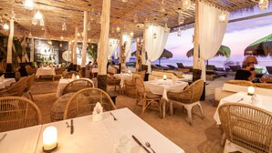 An outdoor restaurant with wicker furniture, white tablecloths, and hanging lanterns.