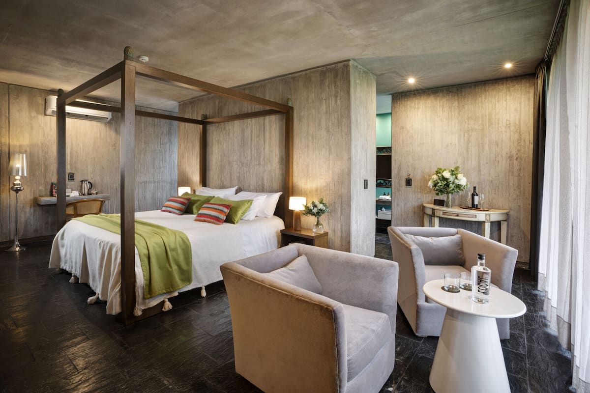 Ein modernes Hotelzimmer mit Himmelbett, einer Sitzecke mit Tisch und einem kleinen Beistelltisch mit Lampe.