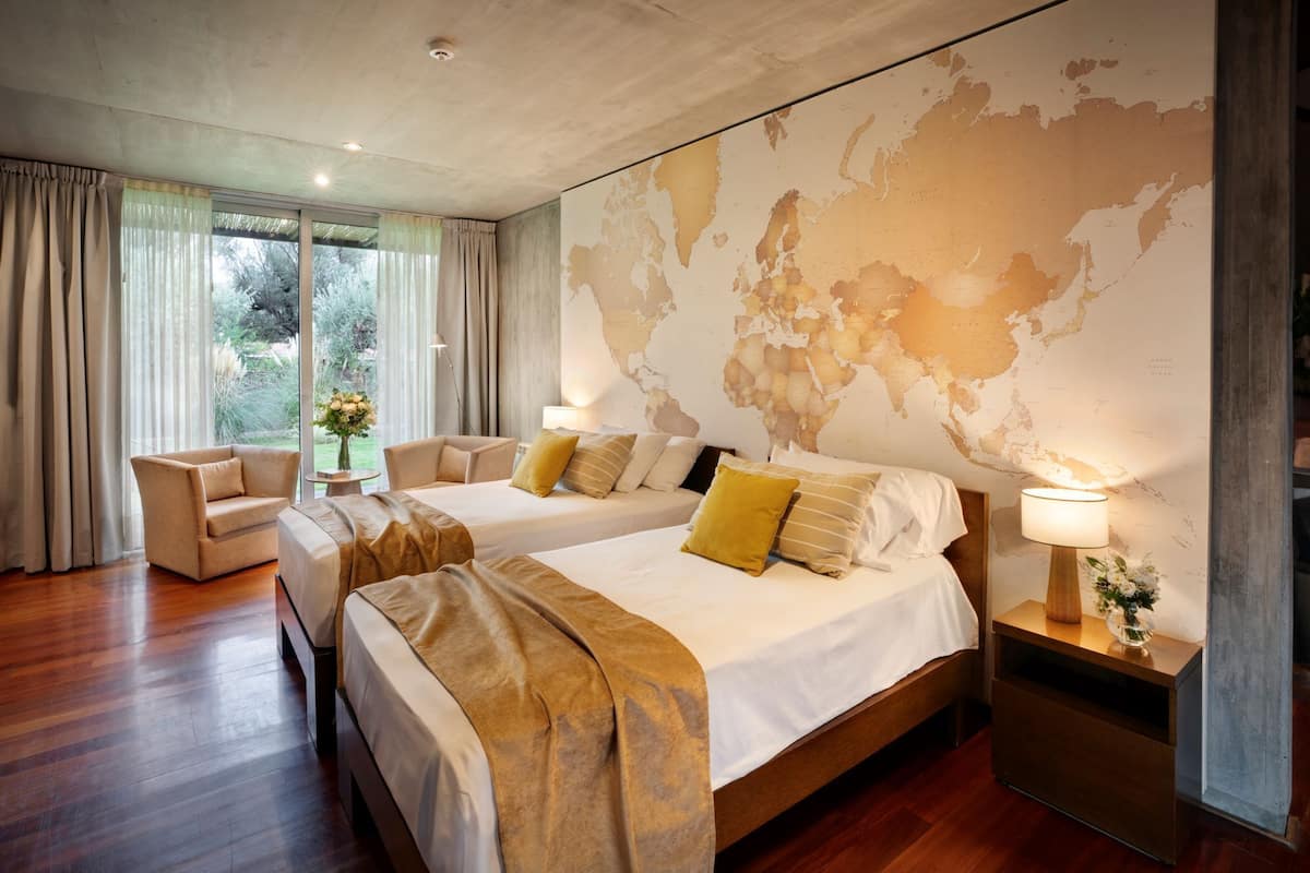 Ein Hotelzimmer mit zwei Betten, einer großen Weltkarte an der Wand, Blick ins Freie und Holzboden.