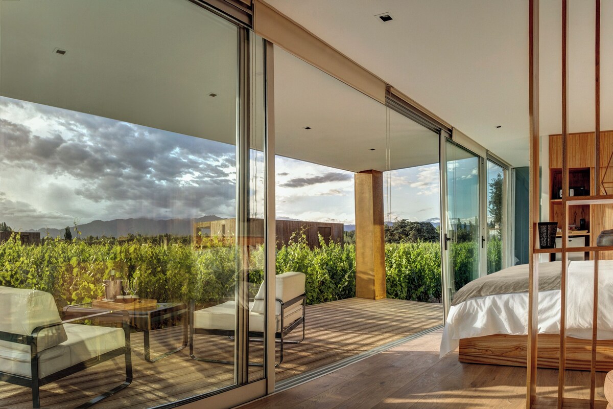 A modern bedroom with a large bed, a glass door leading to a balcony, and a view of the outdoors.