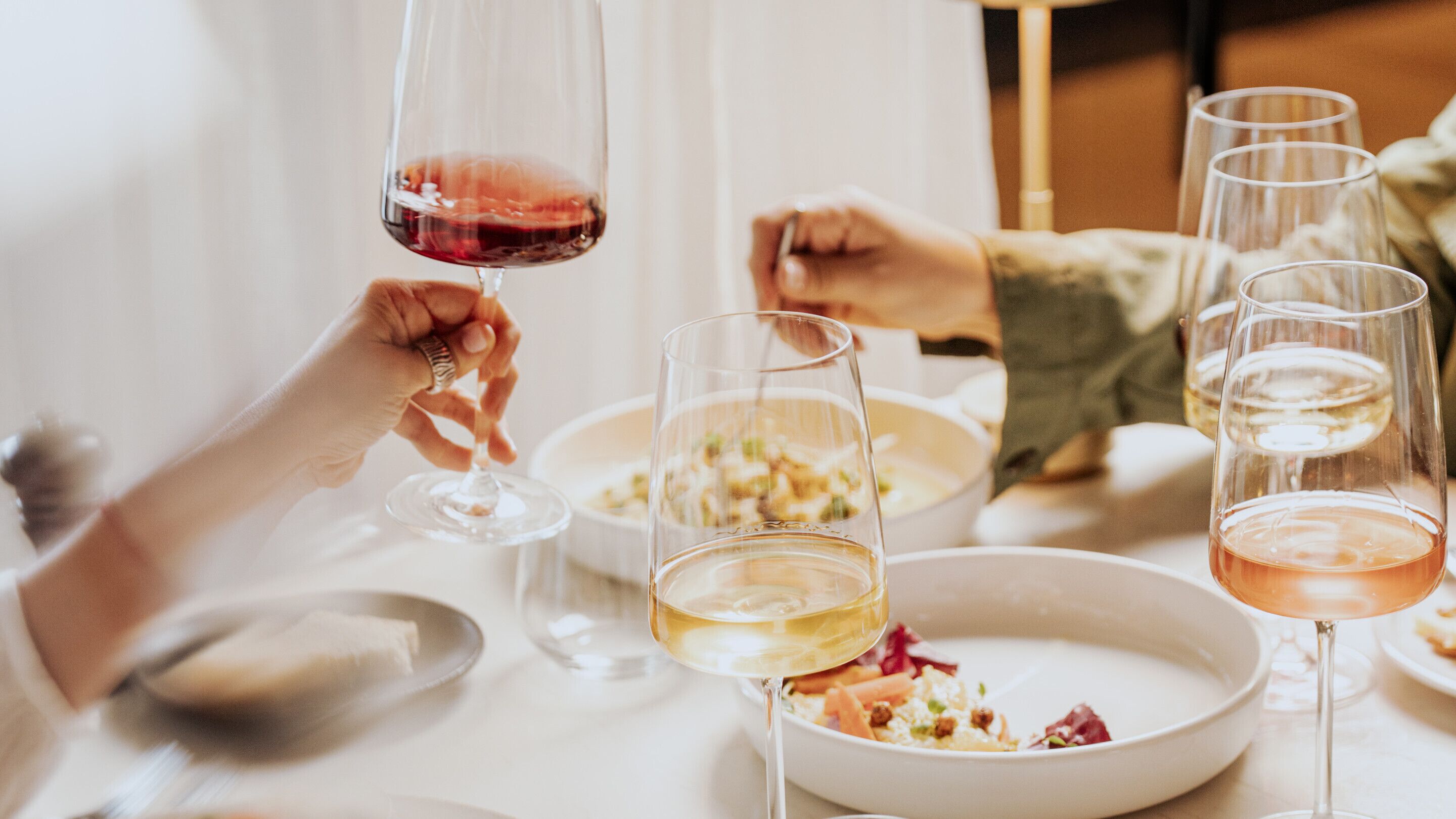 A dining table with multiple glasses of wine, a bowl of salad, and a spoon.