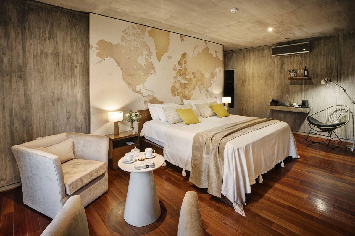 Ein modernes Hotelzimmer mit einem großen Bett, einer Sitzecke mit Tisch und einer Weltkarte an der Wand.