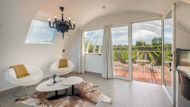Una habitación amplia con techo alto, un candelabro, un gran ventanal que da a una terraza exterior y una alfombra de piel de vaca.