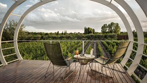 Una terraza de madera con dos sillas verdes y una mesita, con vistas a un viñedo.