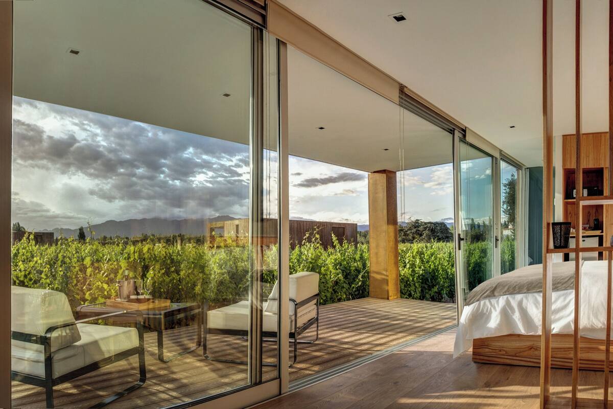 Ein modernes Schlafzimmer mit einem großen Bett, einer Glastür, die auf einen Balkon führt, und Blick ins Freie.