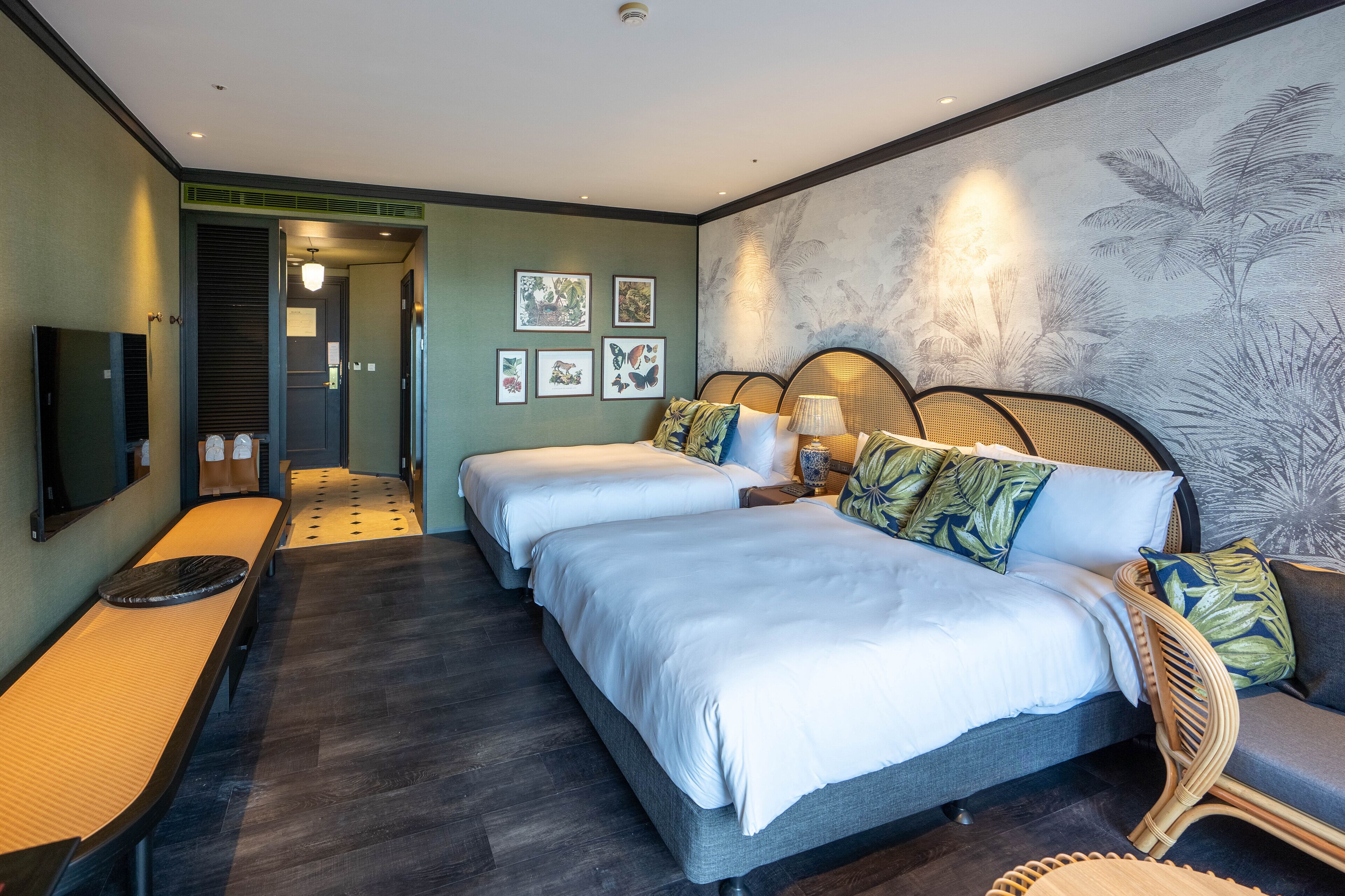 A hotel room with two beds, a sofa, a TV, and artwork on the walls.