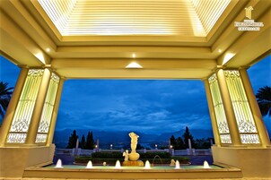 Un espacio al aire libre techado con una fuente, columnas y vista a un paisaje urbano al anochecer.