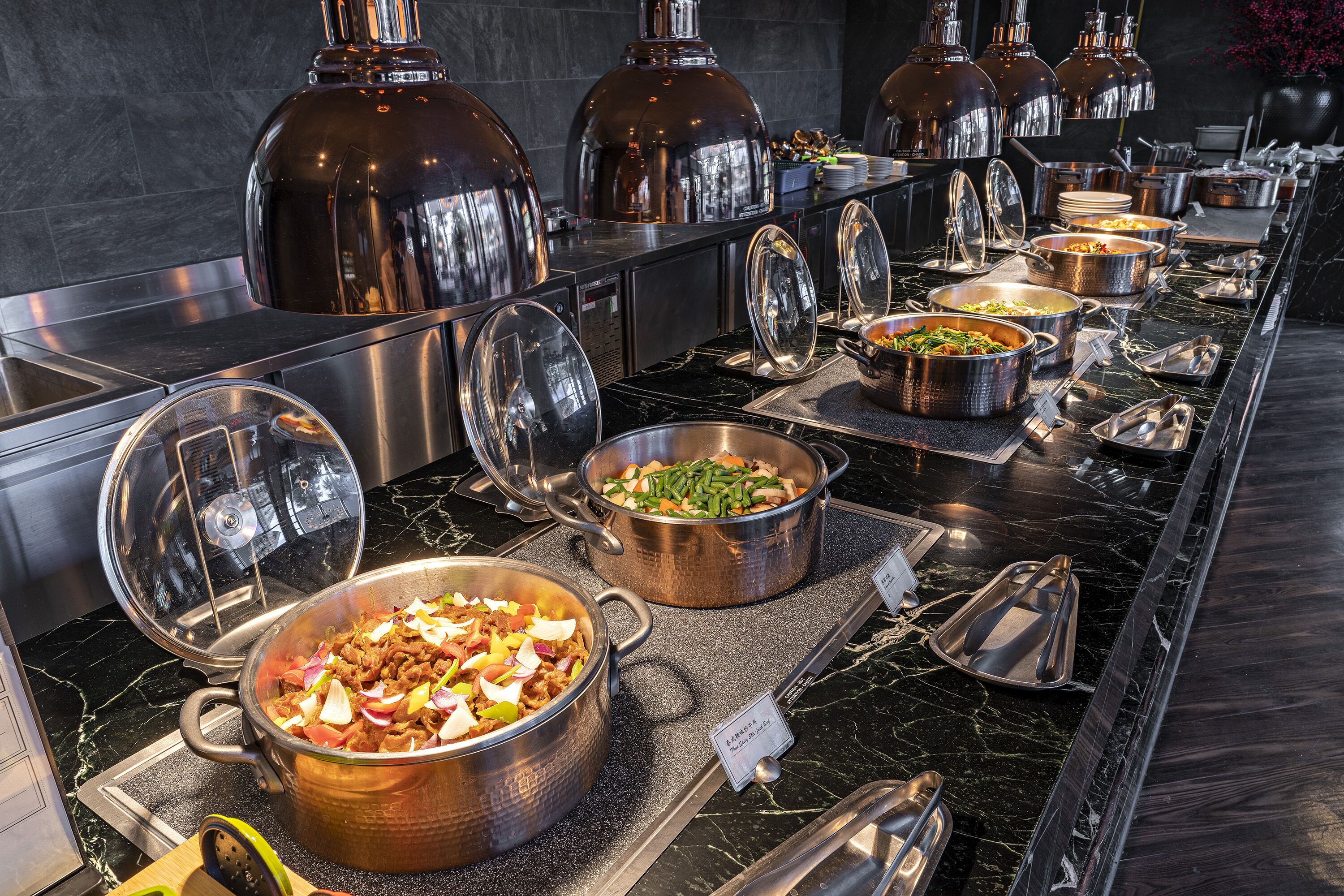 A buffet with various dishes in metal serving containers, a marble countertop, and stainless steel appliances.