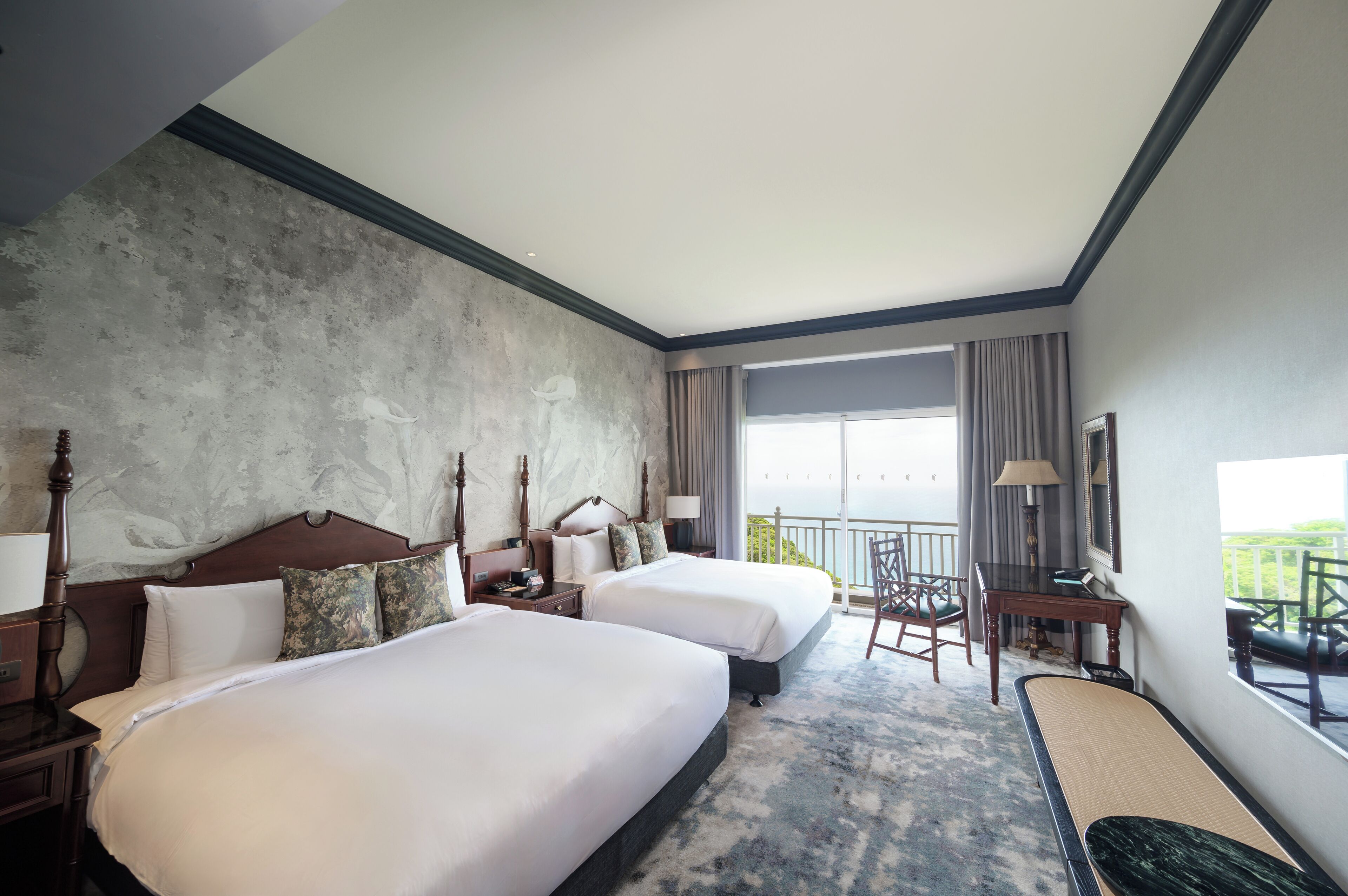 Habitación de hotel con dos camas, un escritorio, una silla y vista al océano.
