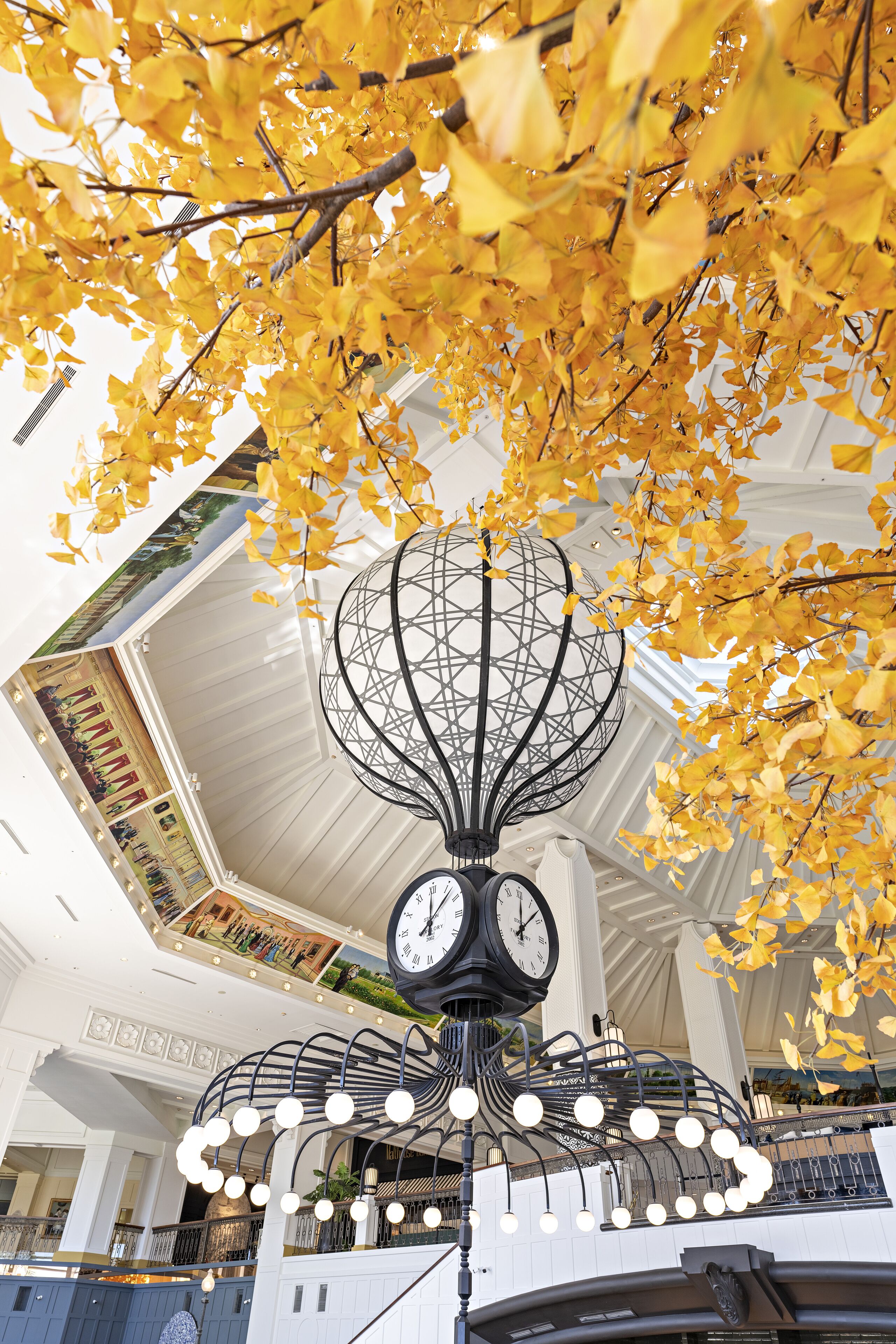 A clock tower with a spherical top, surrounded by hanging lights and yellow leaves.