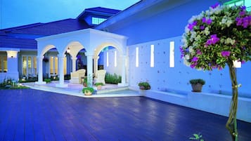 A spacious outdoor area with a wooden deck, white columns, and potted plants.