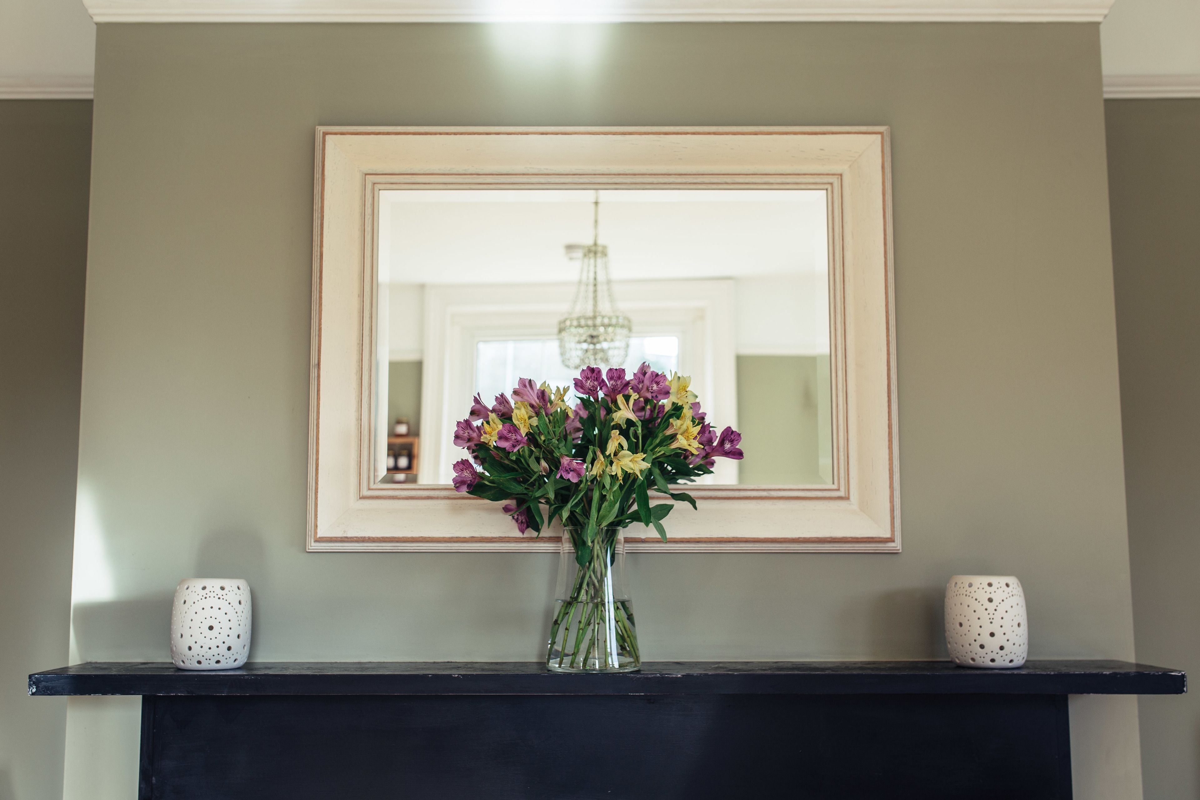 A framed mirror on a wall with a vase of flowers in front of it.