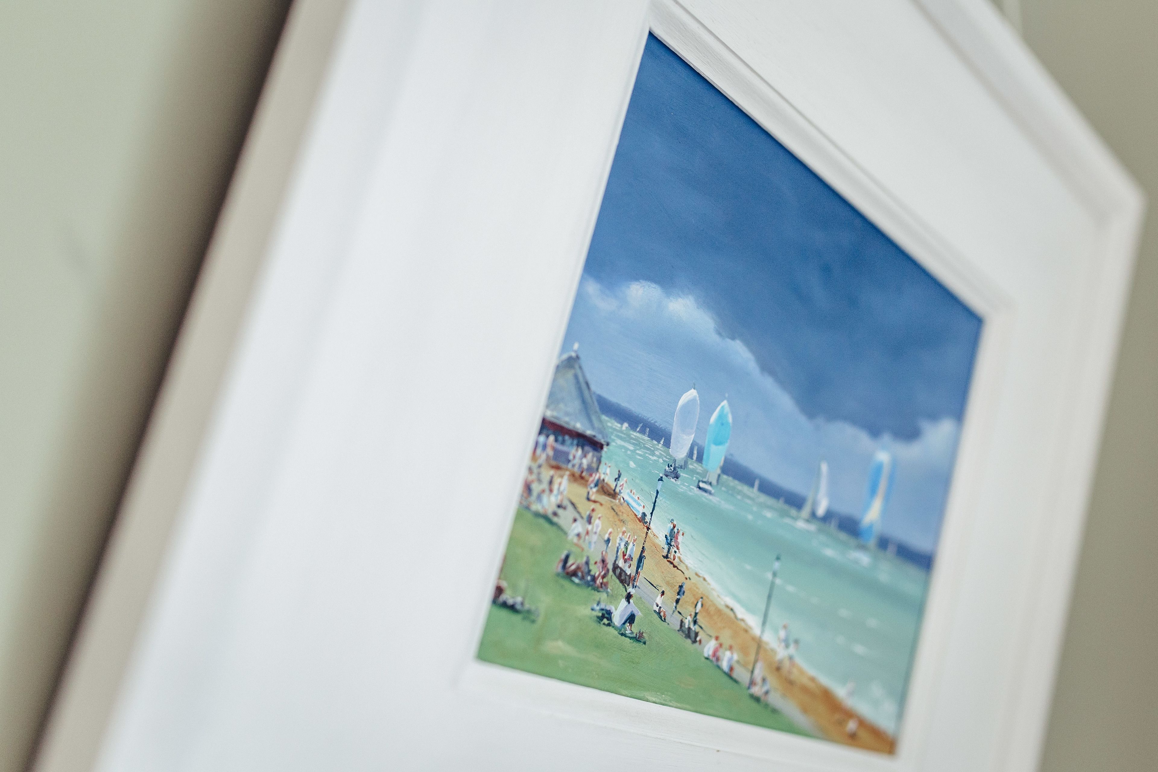 A framed photograph of a beach scene with people, a pier, and sailboats.