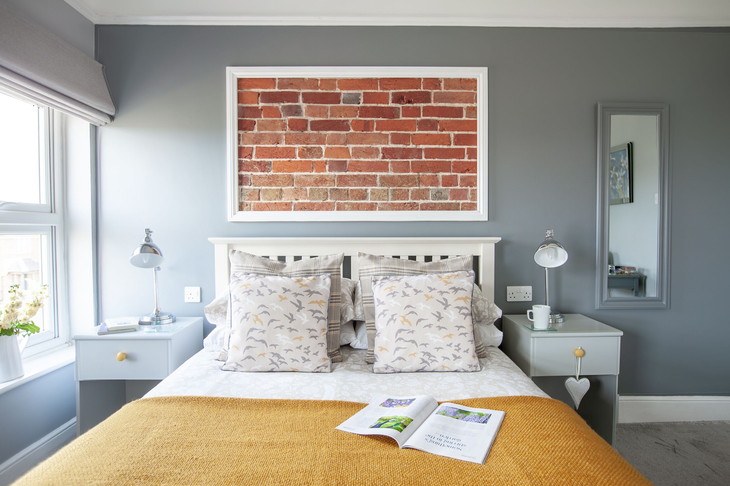 A bedroom with a bed, two nightstands, a window with a view, a wall-mounted artwork, and a bedside table with a lamp.