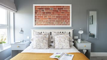 A bedroom with a bed, two nightstands, a window with a view, a wall-mounted artwork, and a bedside table with a lamp.