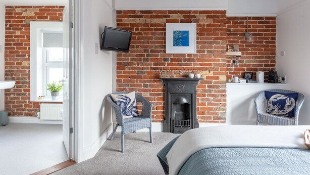 Ein Schlafzimmer mit Backsteinwand, Kamin, Fernseher und zwei Korbstühlen.