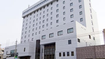Un hotel de varios pisos con diseño moderno, que cuenta con una entrada destacada y un área de piscina visible al frente.