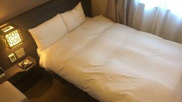 A neatly made bed with white linens, a bedside table with a lamp, and a wall-mounted light fixture.