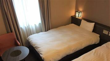 Een hotelkamer met een enkel bed, een klein rond tafeltje en een stoel.