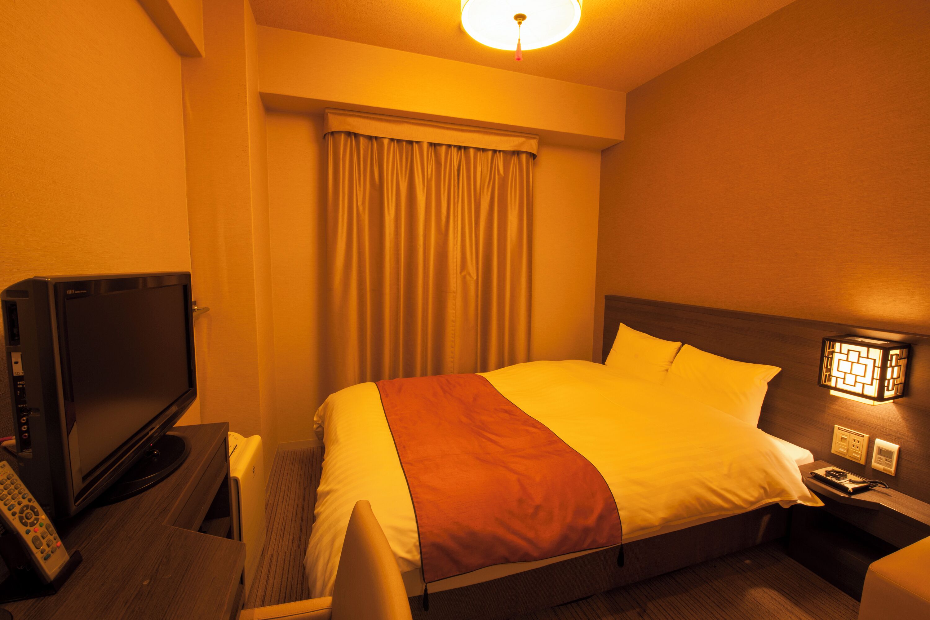 A hotel room with a bed, a television, a nightstand, and a lamp.
