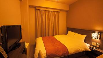 A hotel room with a bed, a television, a nightstand, and a lamp.