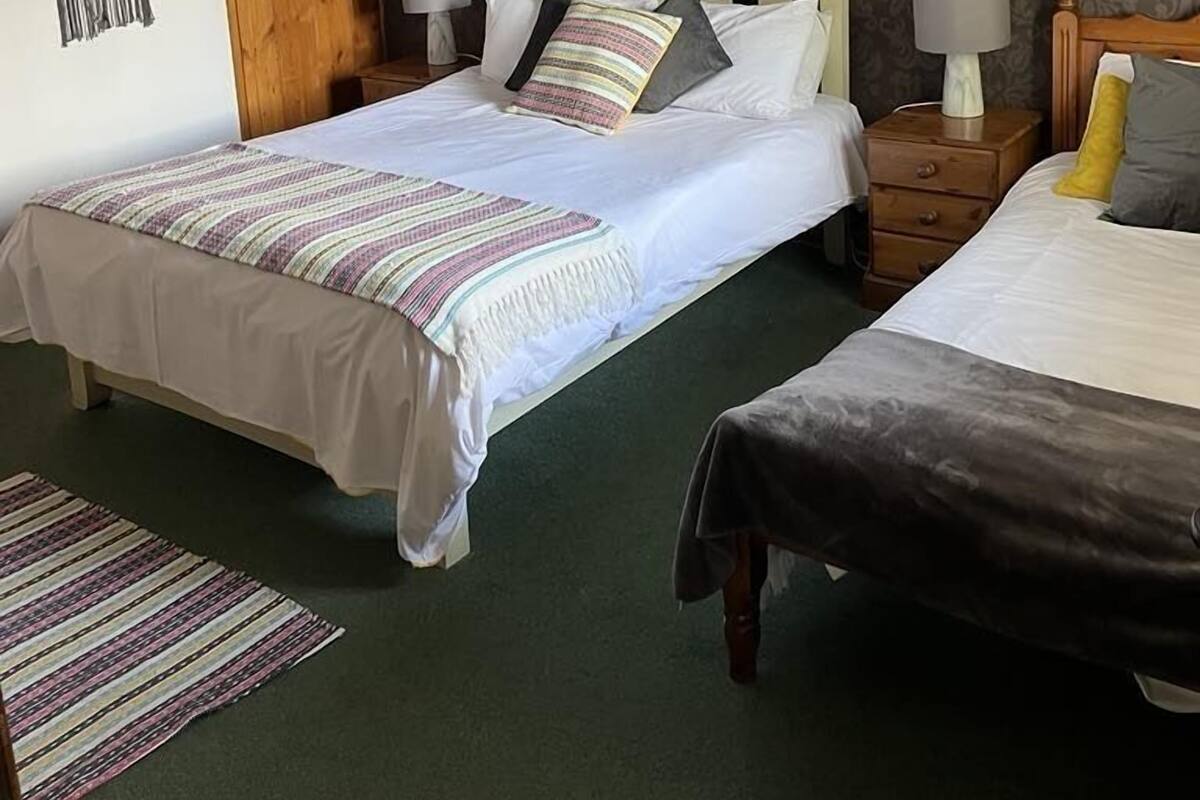 A double bed with a striped blanket, a bedside table with a lamp, and a patterned wall.