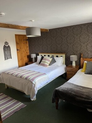 A double bed with a striped blanket, a bedside table with a lamp, and a patterned wall. - The White Horse (Haverhill)