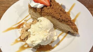A slice of pie with a crumbly topping, a dollop of whipped cream, and a strawberry on top, served on a white plate with caramel sauce drizzled around.