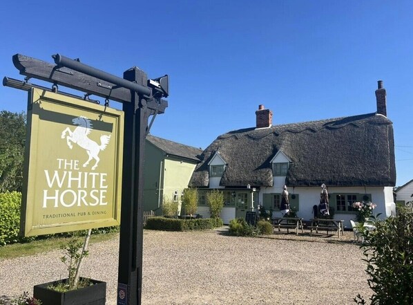 A traditional pub named "The White Horse" with a thatched roof, outdoor seating, and a signboard. - The White Horse (Haverhill)