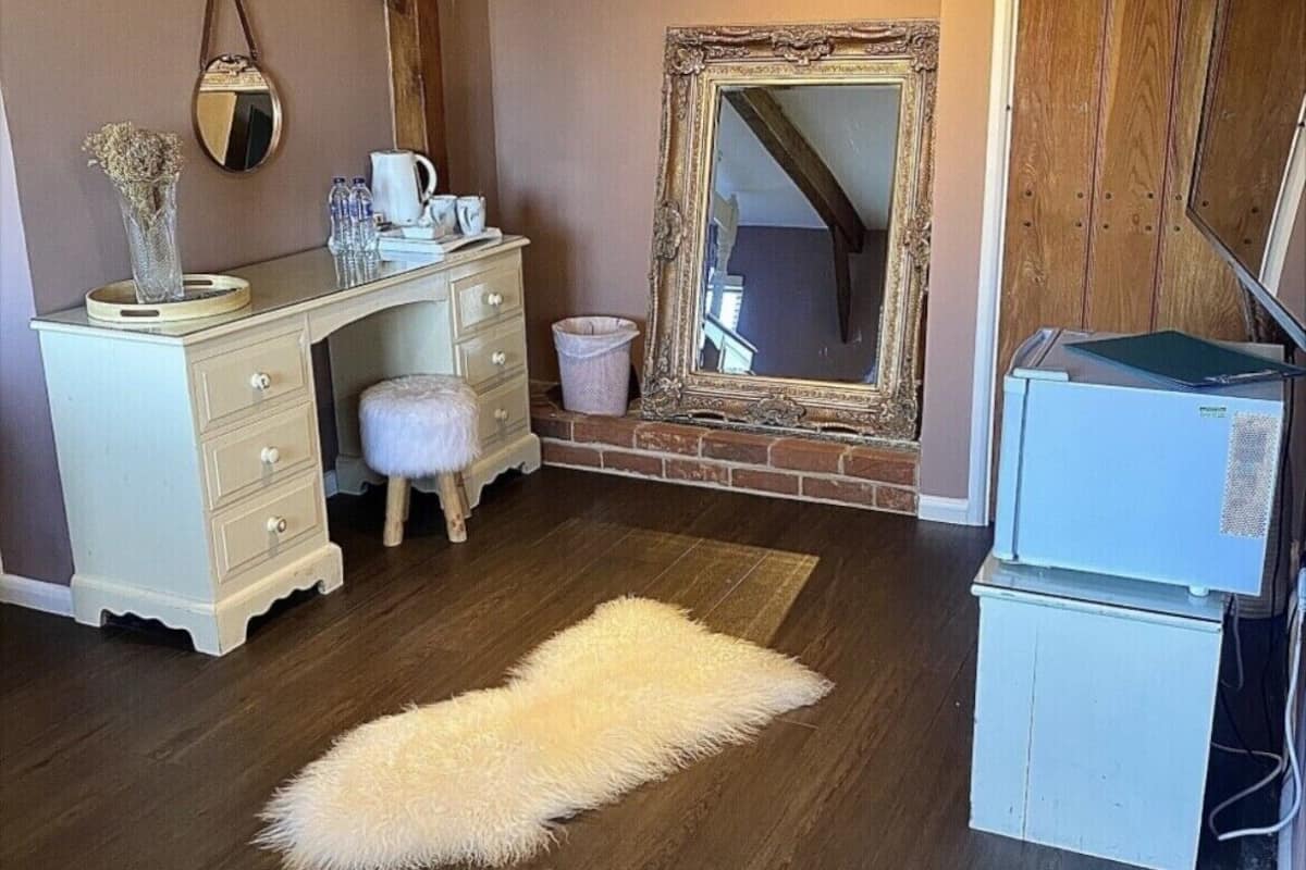 A room with a wooden ceiling, a white dresser, a fluffy rug, a mirror, and a refrigerator.