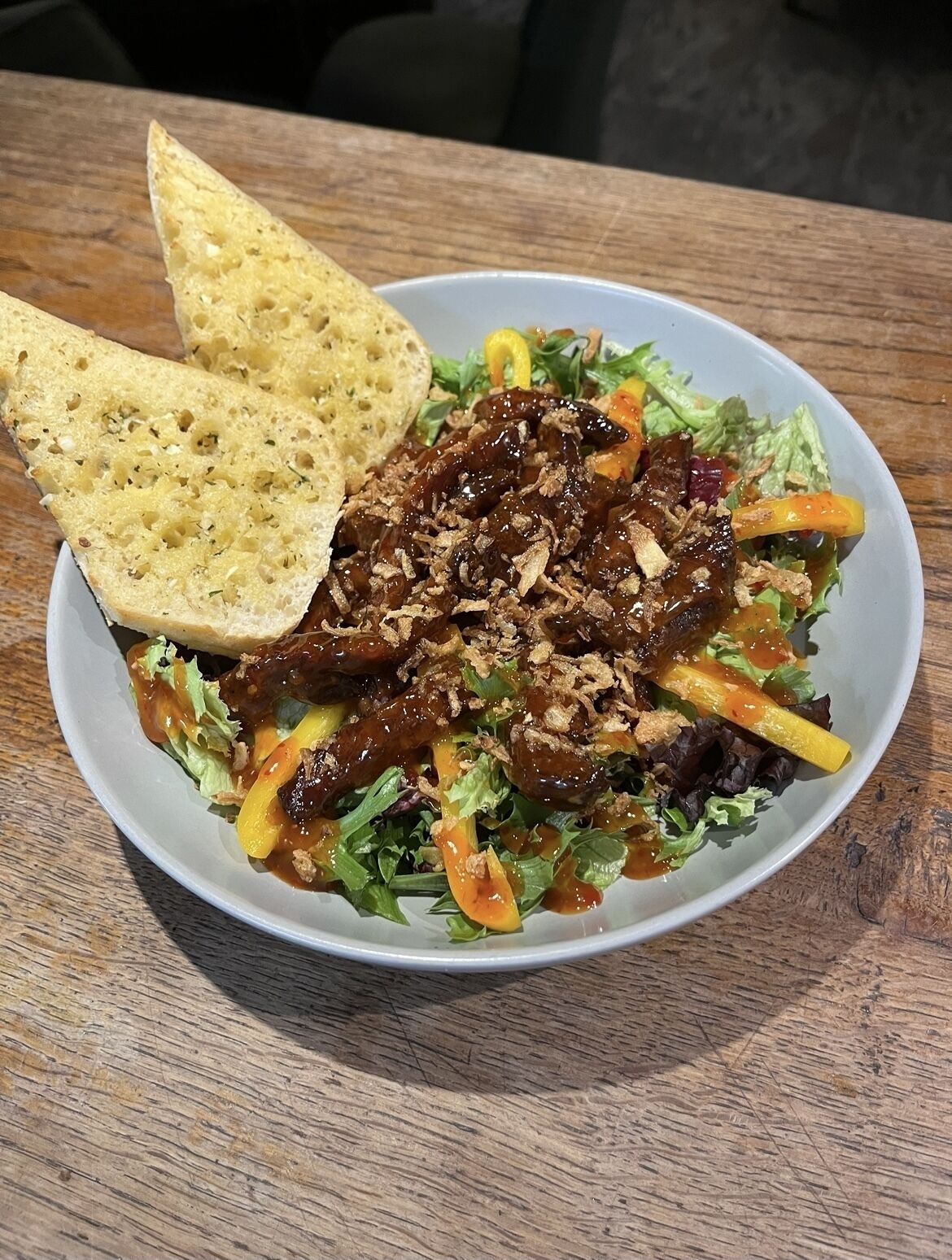 Ein Teller mit Essen, darunter Salat, Fleisch und Brot, auf einem Holztisch.