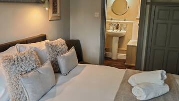 A hotel room with a bed, pillows, a bedside table, a bathroom with a sink and mirror, and a wardrobe.