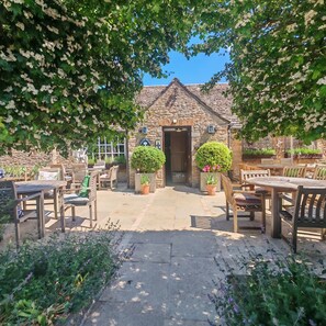 A stone building with a tiled roof, surrounded by outdoor seating and potted plants. - The White Horse Inn (Bicester)